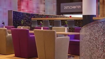 A modern lounge area with sofas and tables, a decorative wall, and a sign reading "ZATSCHRIFTEN".