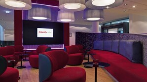 A modern lounge area with red seating, a large screen displaying 'IntercityHotel', and ambient lighting. - IntercityHotel Berlin Hauptbahnhof (Berlin)