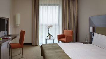 Habitación de hotel con cama, escritorio con silla, una mesita con planta y televisor.