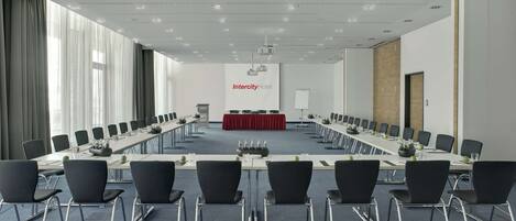 Une salle de conférence avec une longue table, des chaises noires et une nappe rouge.