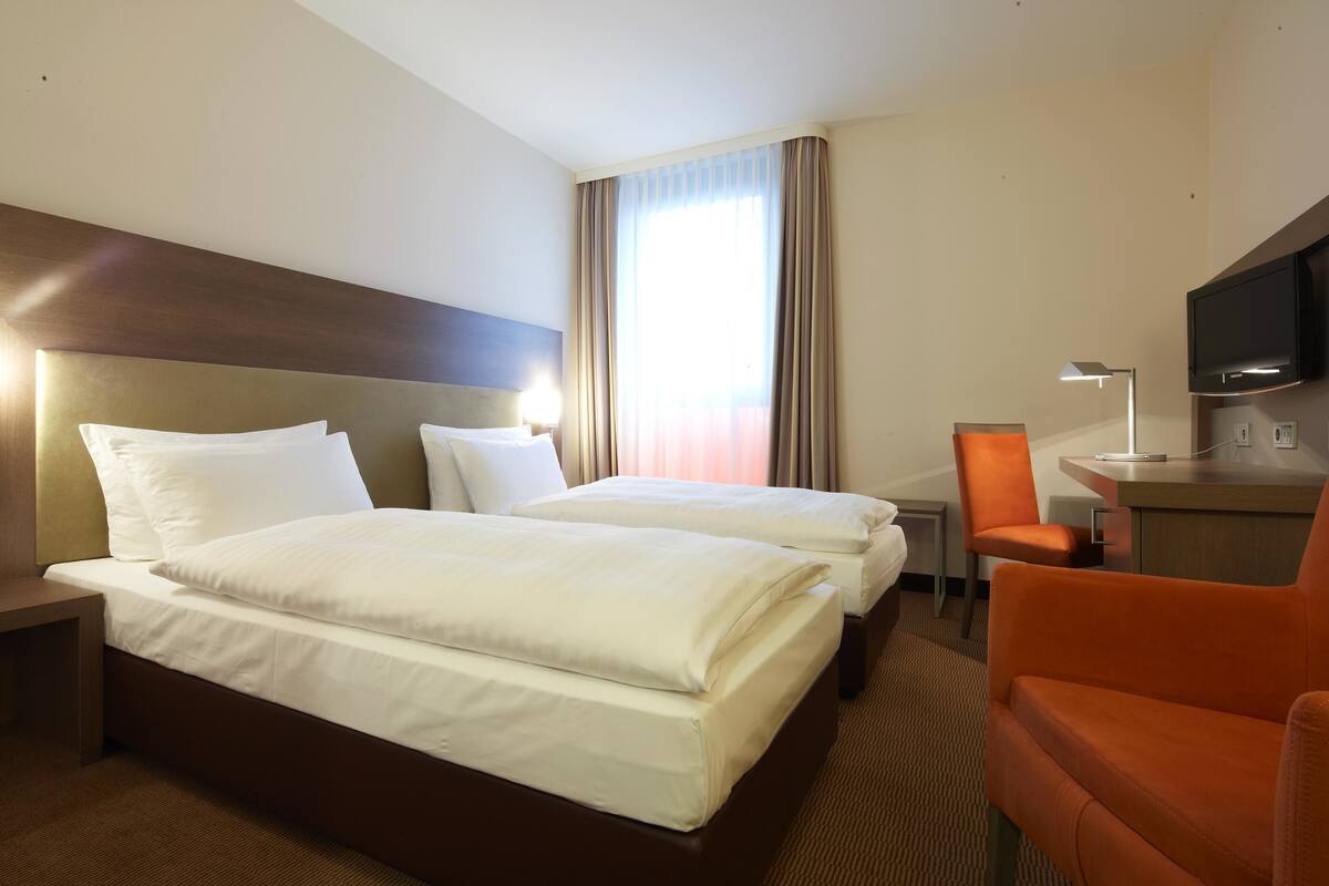 Een hotelkamer met twee bedden, een bureau, een stoel, een televisie en een raam met gordijnen.
