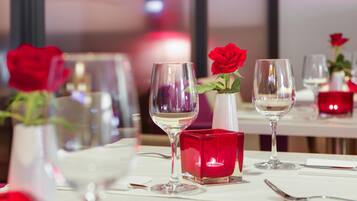 Una mesa de comedor con copas de vino, una vela roja y un florero con una rosa roja.