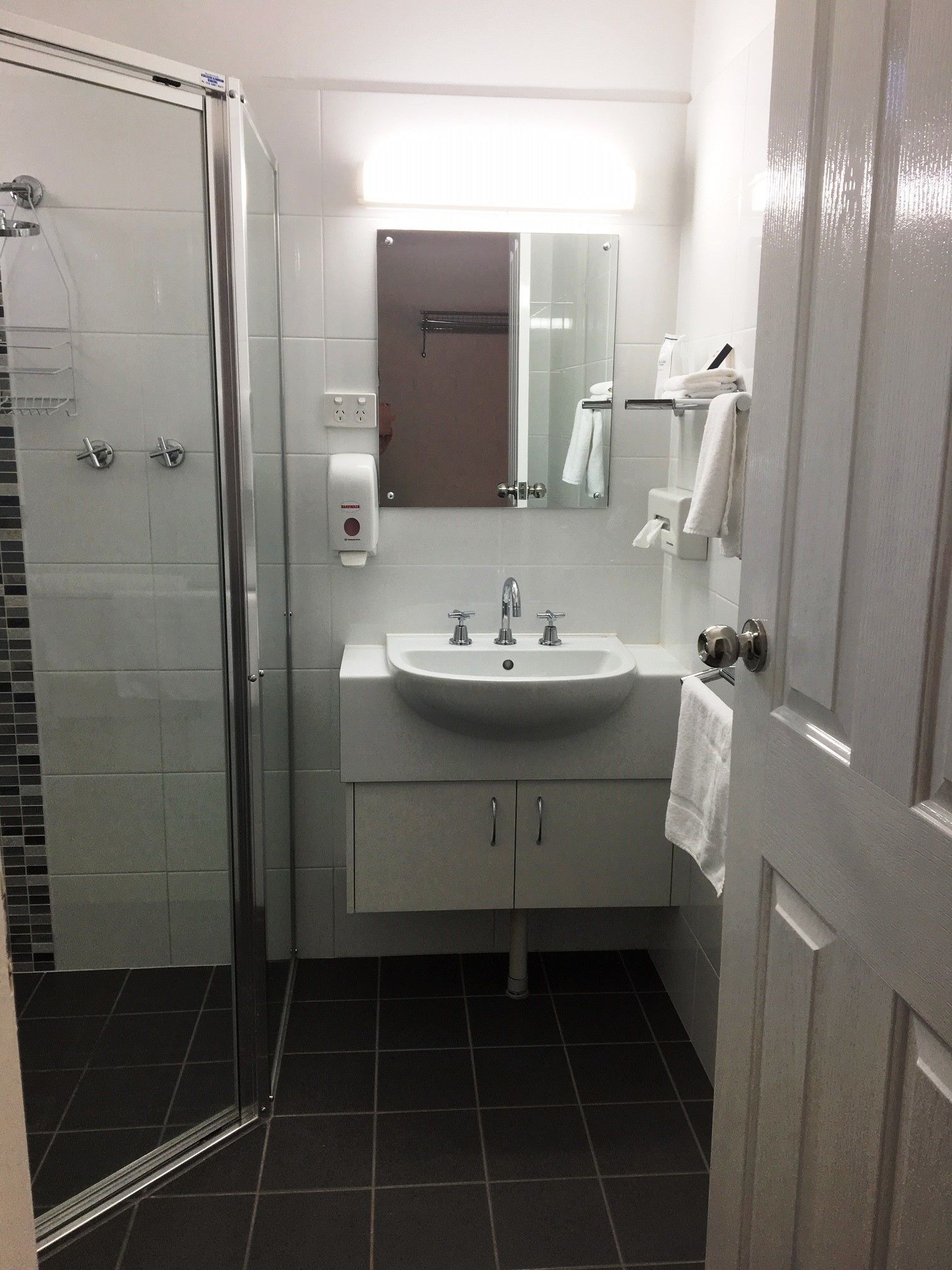 Un bagno moderno con cabina doccia in vetro, un lavandino bianco con due rubinetti e uno specchio sopra il lavandino.