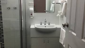 A modern bathroom with a glass shower enclosure, a white sink with two faucets, and a mirror above the sink.