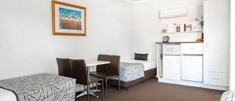 Une chambre avec deux lits, une table à manger avec des chaises, un coin cuisine et un tableau encadré au mur.