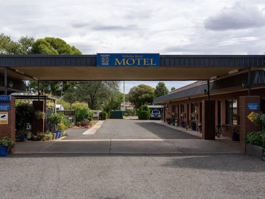 Un motel con entrada techada, un cartel y un estacionamiento.