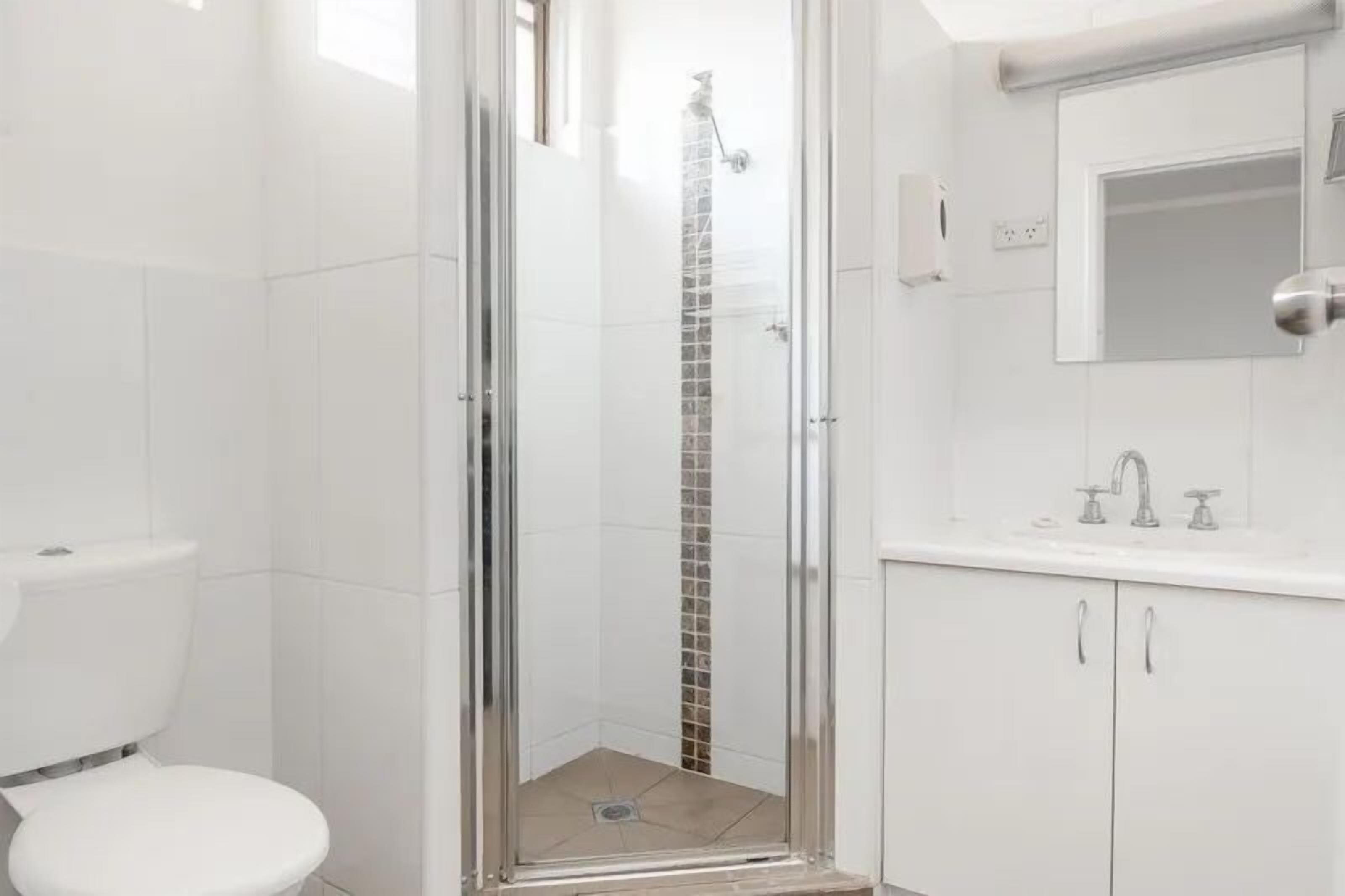 A bathroom with a glass-enclosed shower, a toilet, and a sink with a mirror above it.