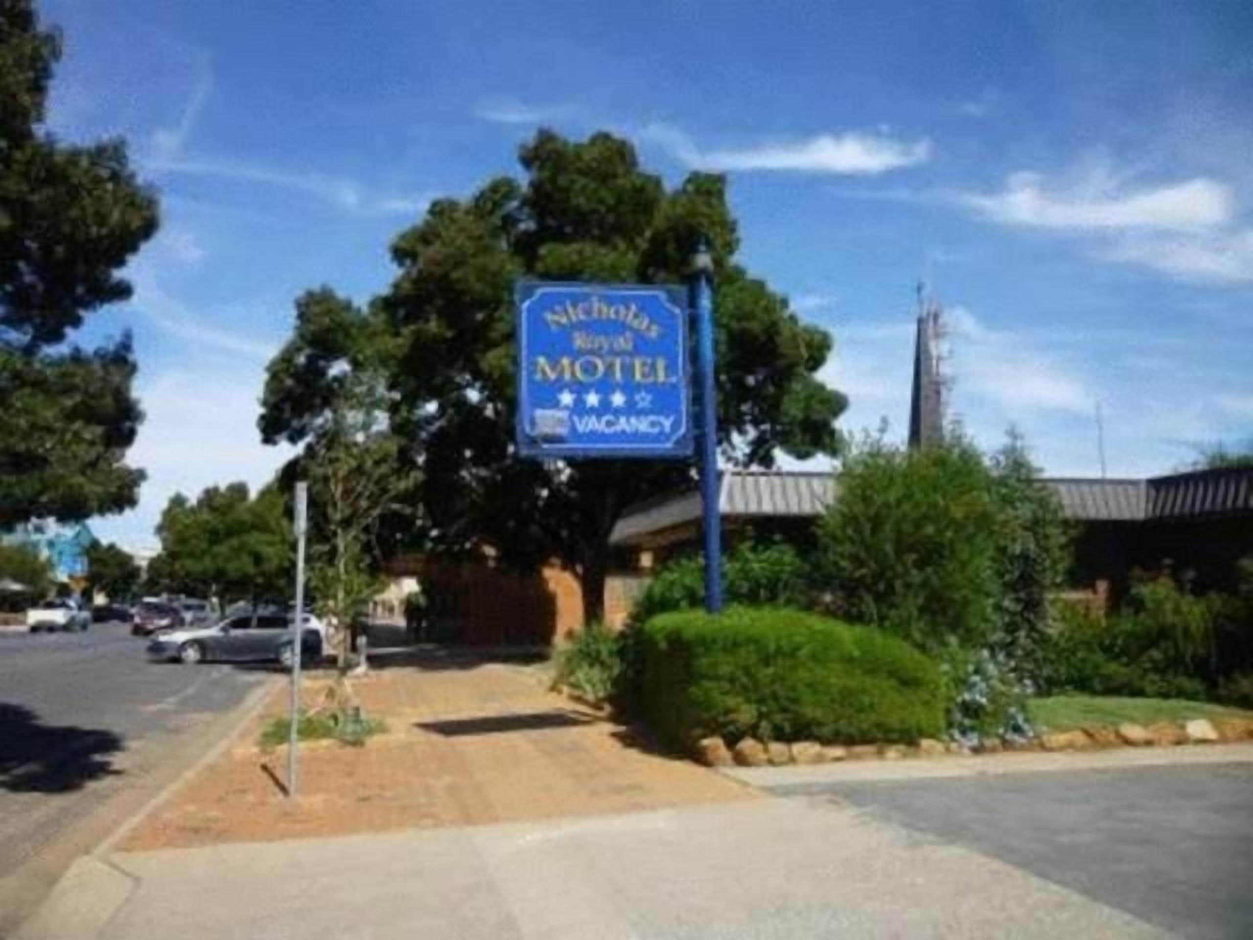 A motel with a blue sign, a parking lot, and a building with a sloped roof.