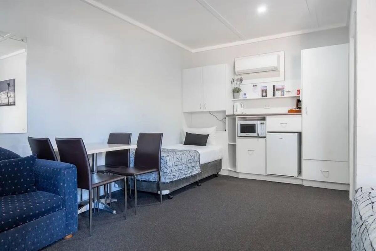 A compact room with a bed, a small kitchenette, a dining table with chairs, and a sofa.