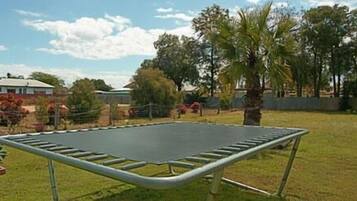 A trampoline in a grassy yard with trees and a building in the background.