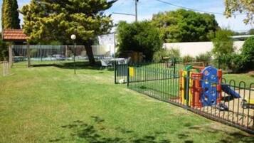 A fenced outdoor area with a playground, including a slide and climbing structures.
