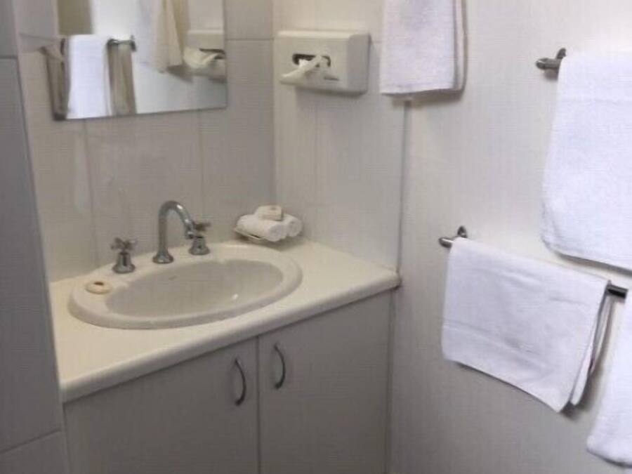 Une petite salle de bain propre, équipée d’un lavabo, d’un miroir, d’un porte-serviettes et d’un distributeur de papier toilette.