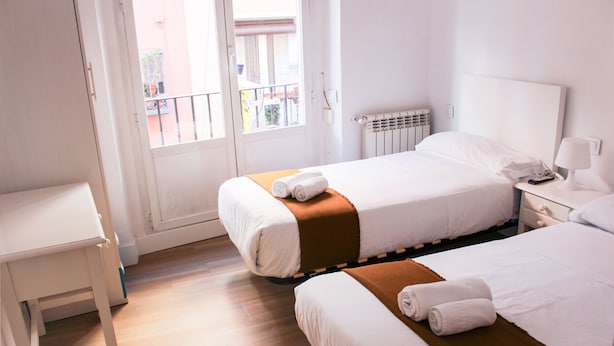 A hotel room with two beds, a small table, a nightstand, and a window with a view of the outside. - Pensión MYD La Estrella (Madrid)