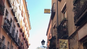 A narrow street with buildings on either side, featuring balconies with plants and a sign for a restaurant. - Pensión MYD La Estrella (Madrid)