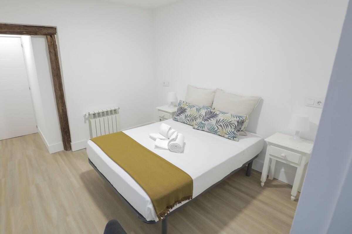 A hotel room with a bed, a bedside table, a nightstand, a radiator, and a door.