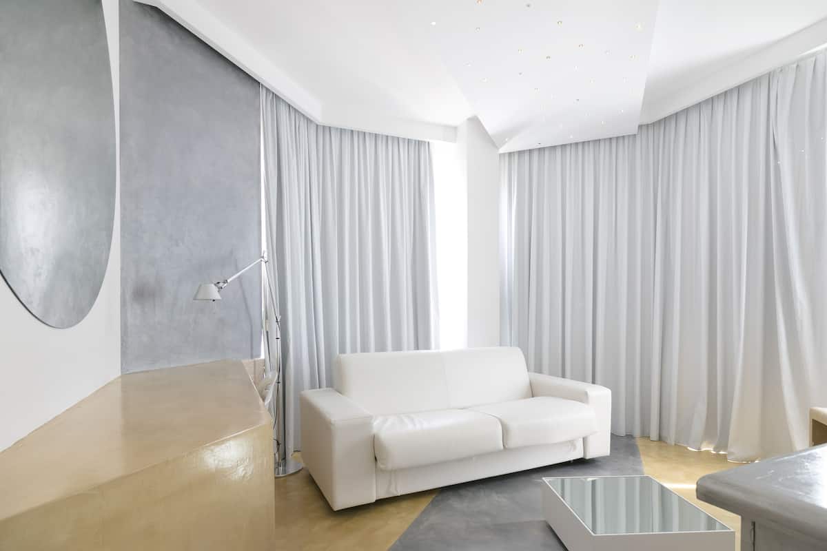 Una sala de estar moderna con un sofá blanco, una mesa de centro de vidrio y un ventanal con cortinas.