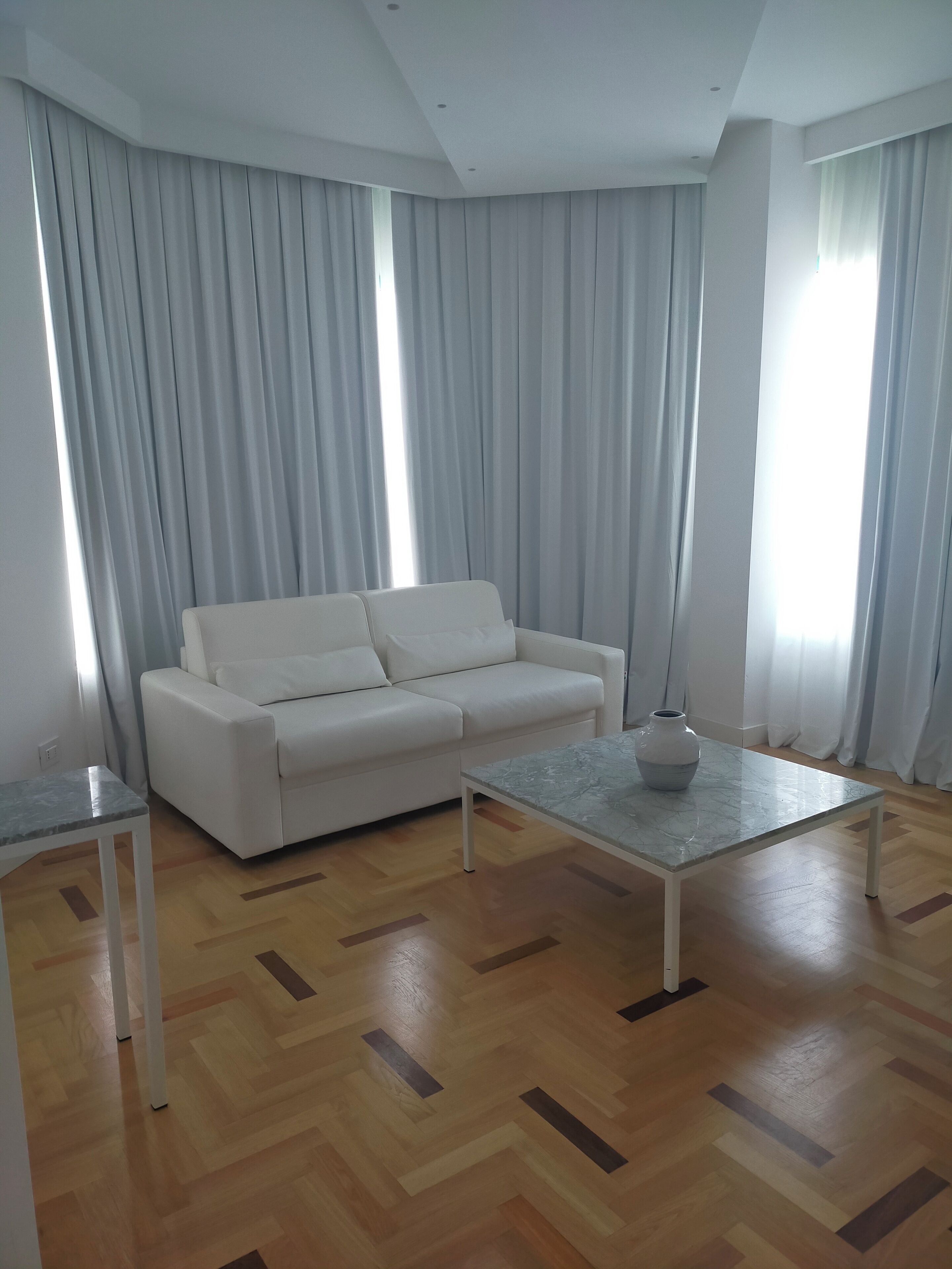 A modern living room with a white sofa, a marble coffee table, and a wooden parquet floor.