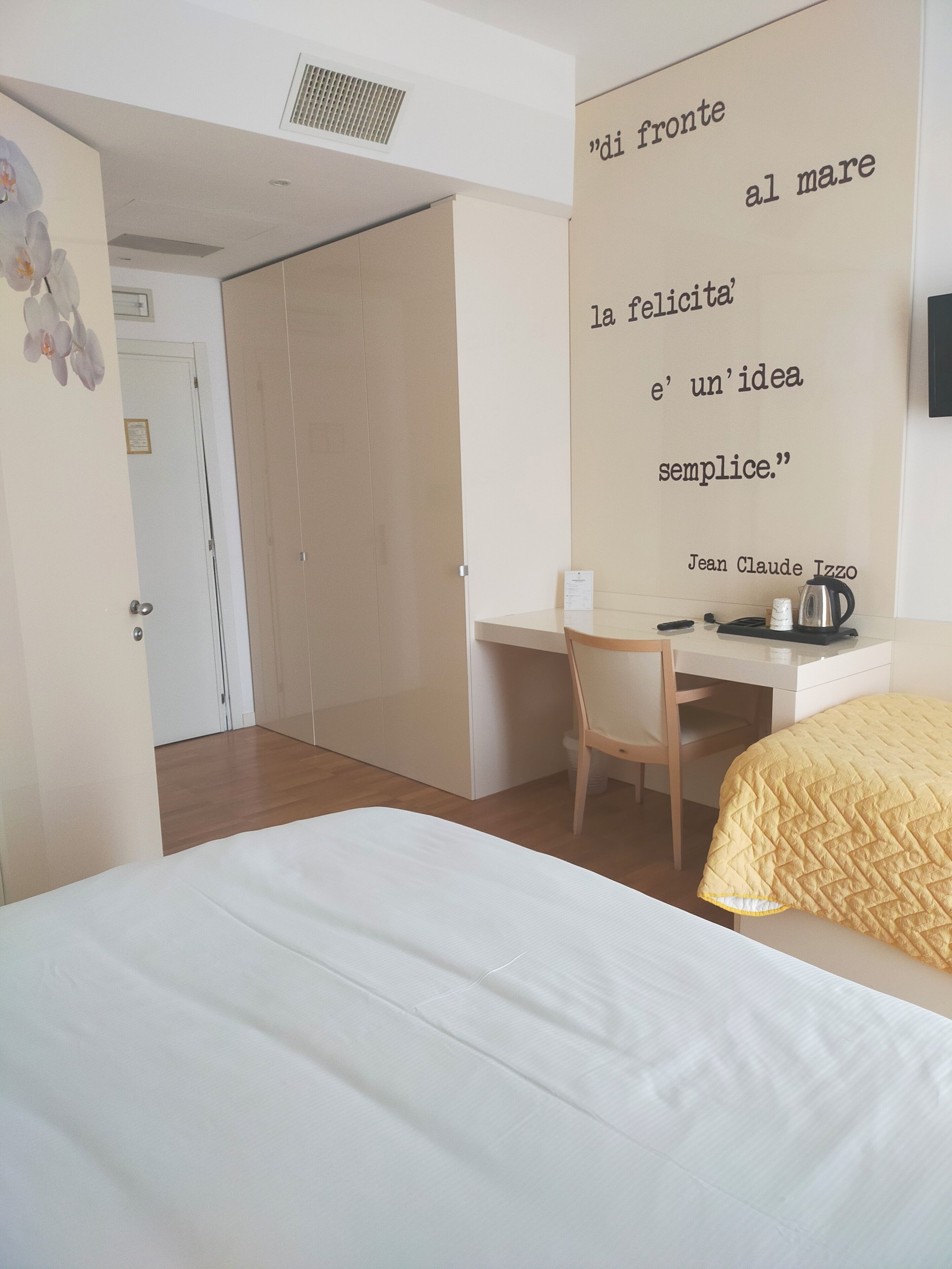 A bedroom with a bed, a desk, and a chair. There is a quote on the wall and a door in the background.