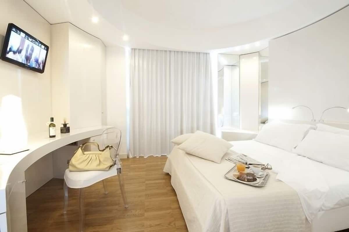 Una habitación de hotel moderna con cama, mesita de noche, televisor y una silla.