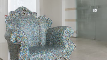 Un fauteuil à l’esthétique originale, placé dans un hall d’entrée moderne, avec un panneau indiquant « PRENEZ VOTRE SELFIE ICI » au sol.