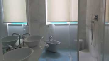 A modern bathroom with a large mirror, two sinks, a bidet, and a glass-enclosed shower.