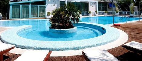 A swimming pool with a central island, surrounded by lounge chairs and a wooden deck.