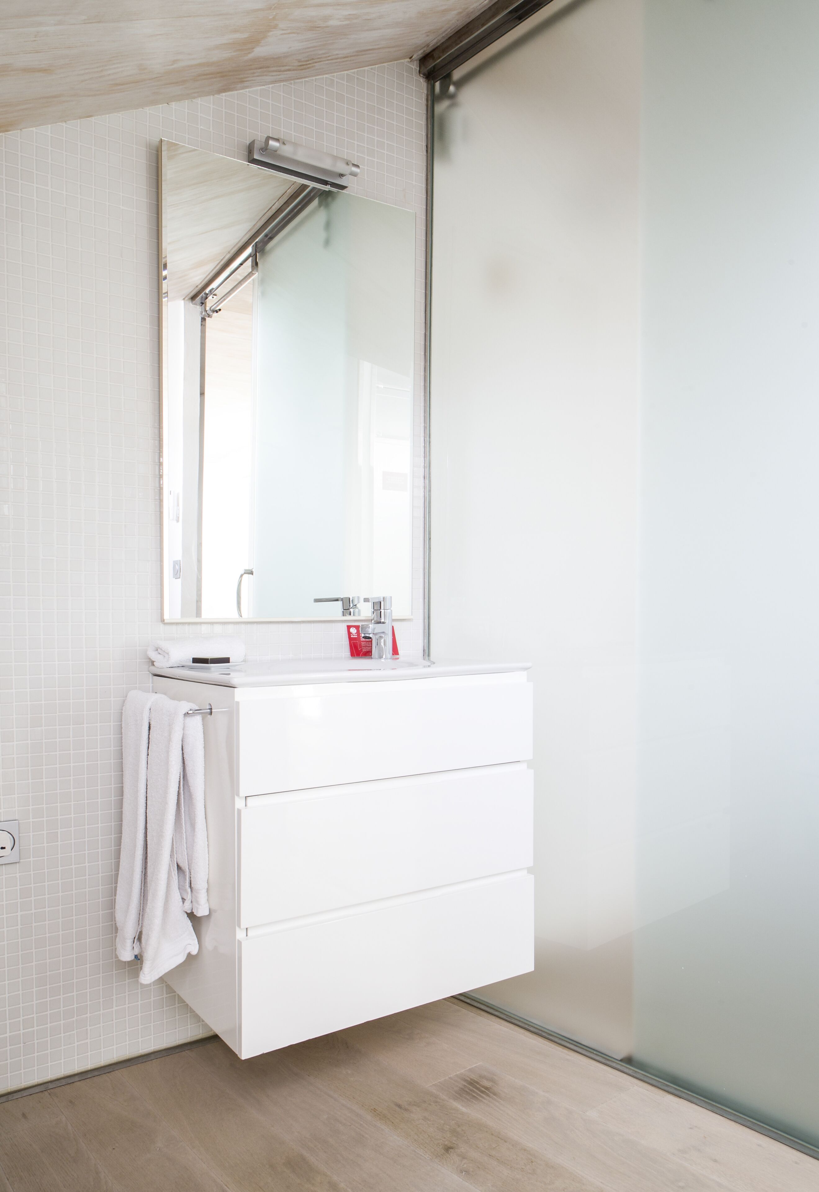 Une salle de bain moderne avec un meuble-lavabo blanc, un grand miroir et une serviette accrochée au mur.