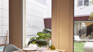 A modern dining area with a table and chairs, large windows, and a view of a garden and building outside. - La Alcoba del Agua Hotel Boutique (Sanlucar de Barrameda)