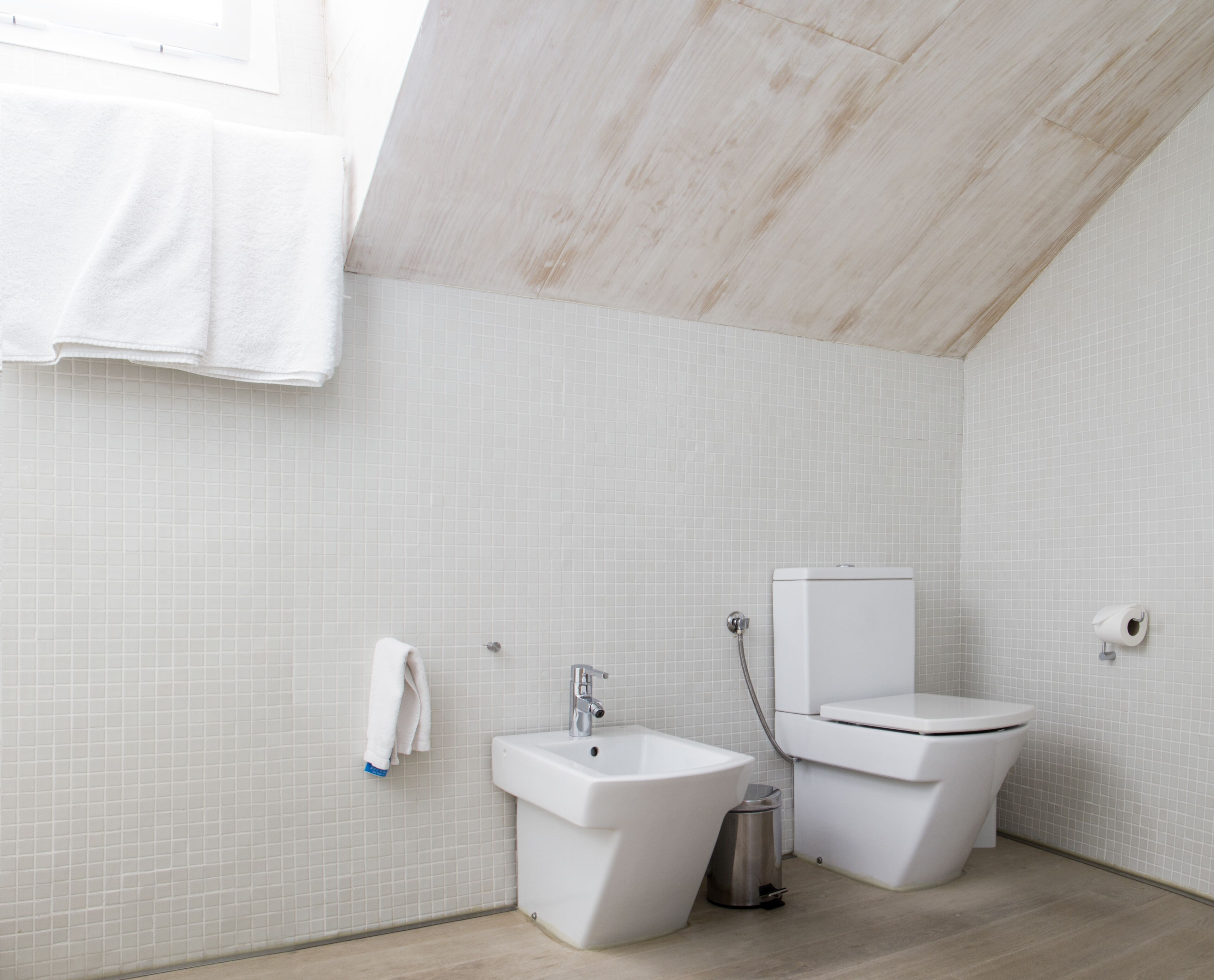 Un baño moderno con azulejos blancos, un bidé, un inodoro y un lavabo.
