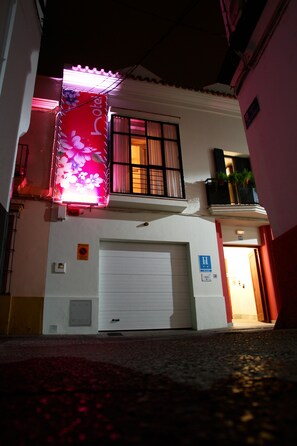 A hotel with a closed garage door, a balcony with a flower-patterned awning, and a visible entrance door. - La Alcoba del Agua Hotel Boutique (Sanlucar de Barrameda)