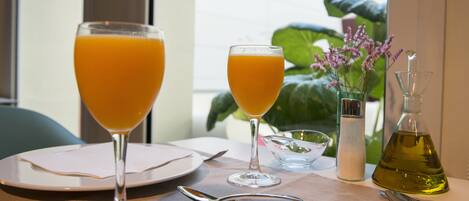 A table set with two glasses of orange juice, a salt and pepper shaker, a small bowl, and a bottle of olive oil.