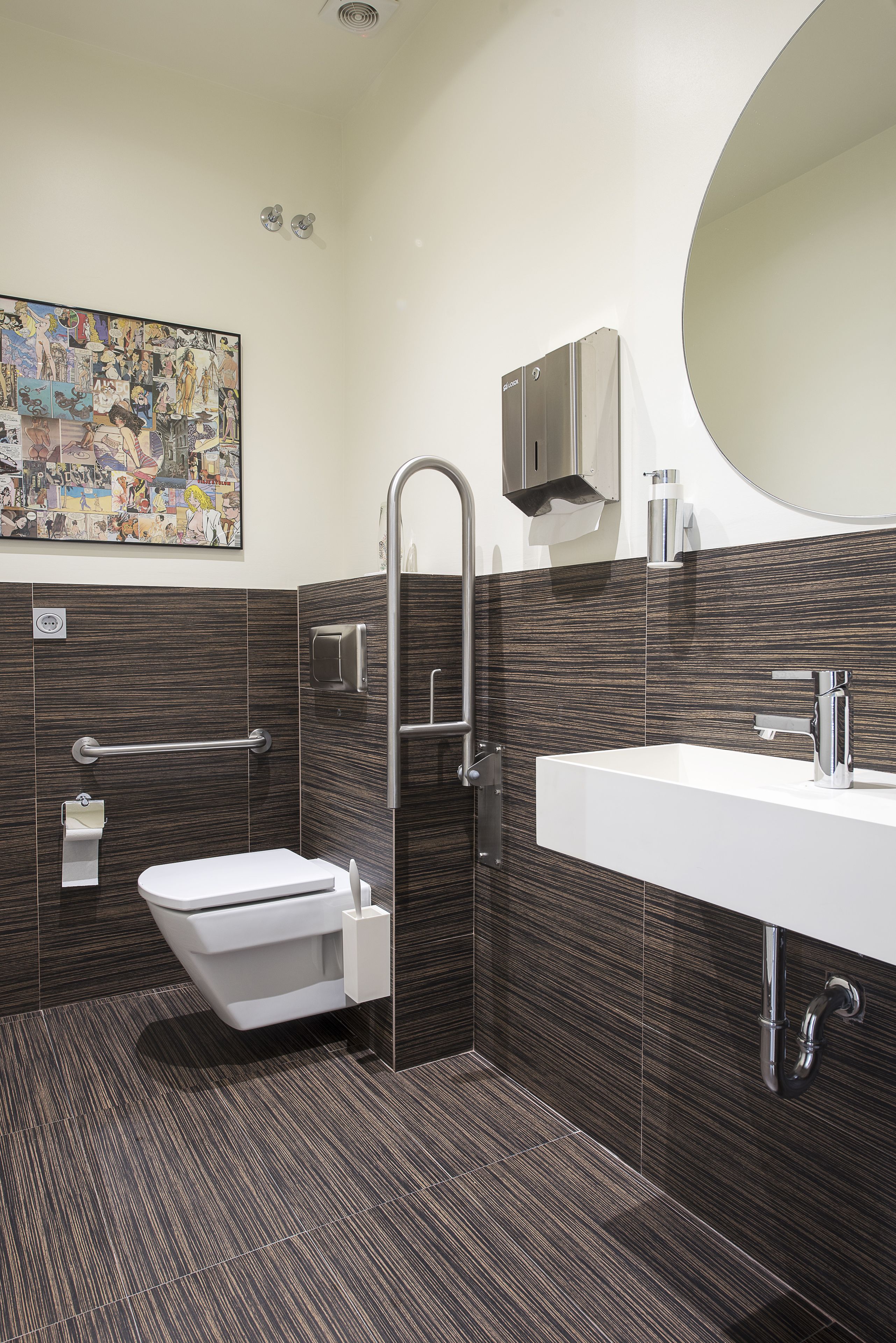 A modern bathroom with a toilet, bidet, and sink, featuring dark patterned tiles and a large mirror.