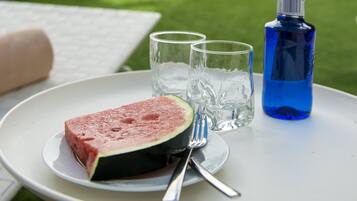 A table with a slice of watermelon, two glasses, a fork, and a blue water bottle.