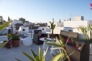 A rooftop terrace with wicker furniture, potted plants, and a white table. - La Alcoba del Agua Hotel Boutique (Sanlucar de Barrameda)