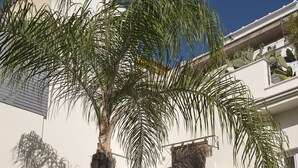 A building with a balcony, palm trees, and a clear blue sky. - La Alcoba del Agua Hotel Boutique (Sanlucar de Barrameda)