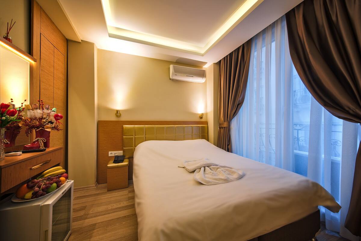 A hotel room with a bed, bedside table, and a small desk with a lamp.
