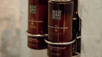 Duas embalagens de shampoo e gel de banho 'The Rituals of Happy Buddha' sobre uma parede de mármore.