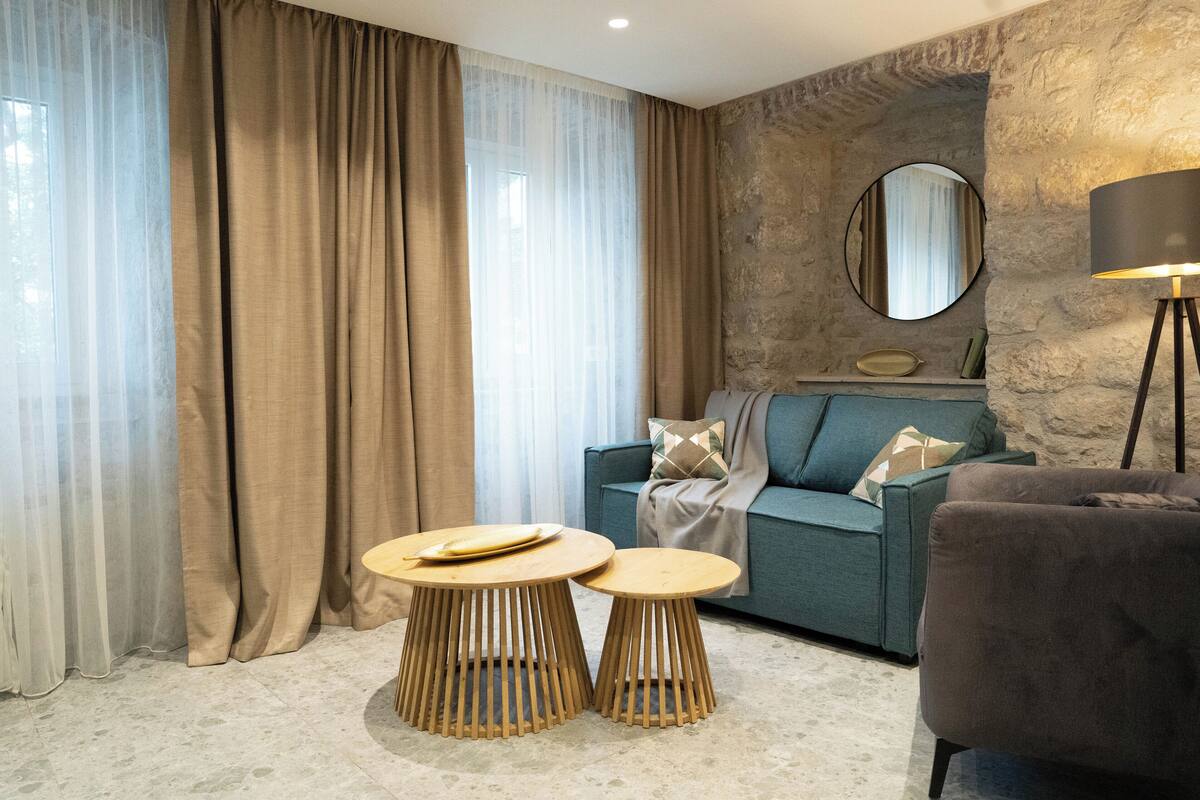A modern living room with a sofa, two wooden side tables, a lamp, and a stone accent wall.