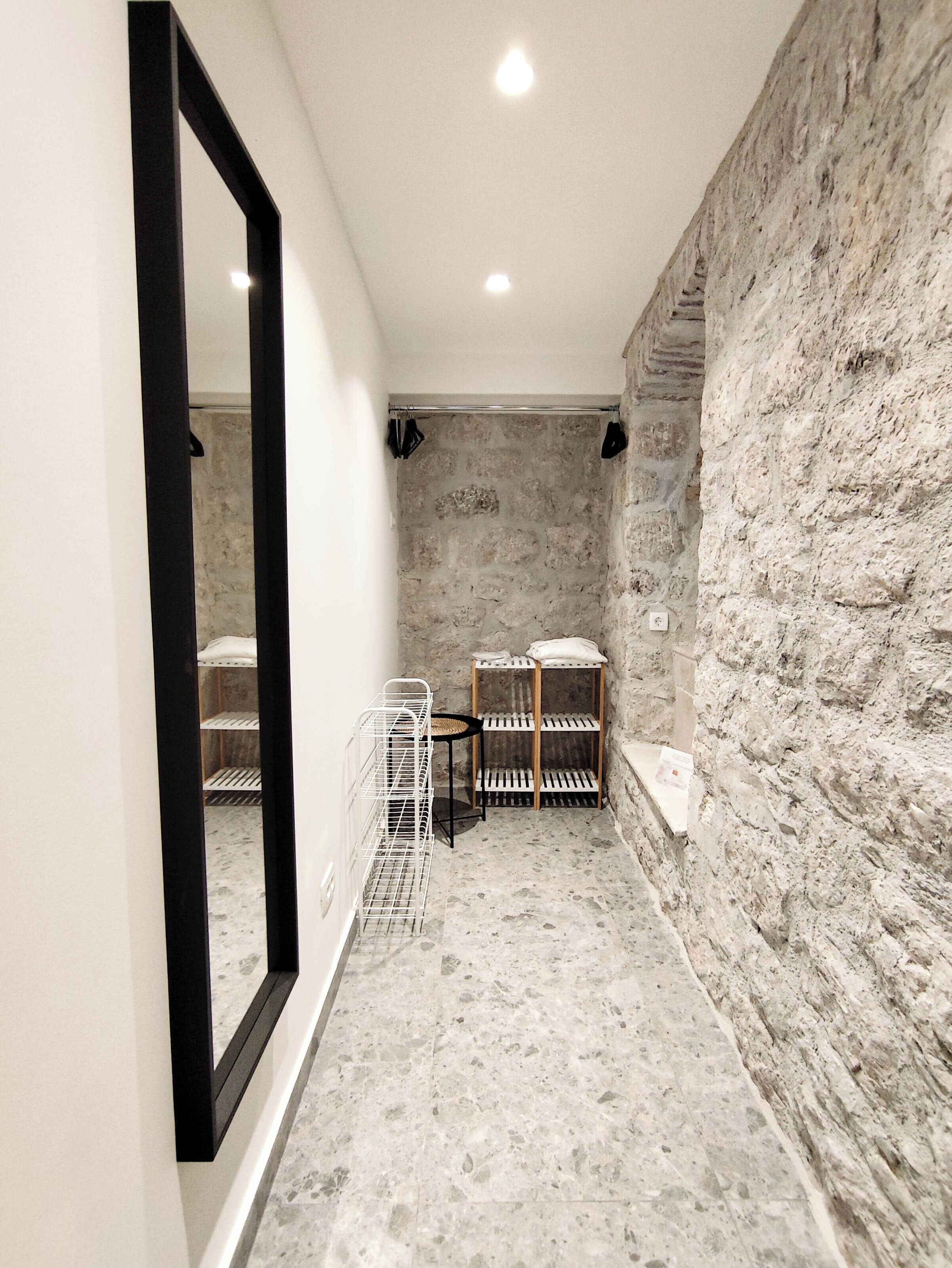 A narrow hallway with a stone wall, a metal rack, and a mirror.
