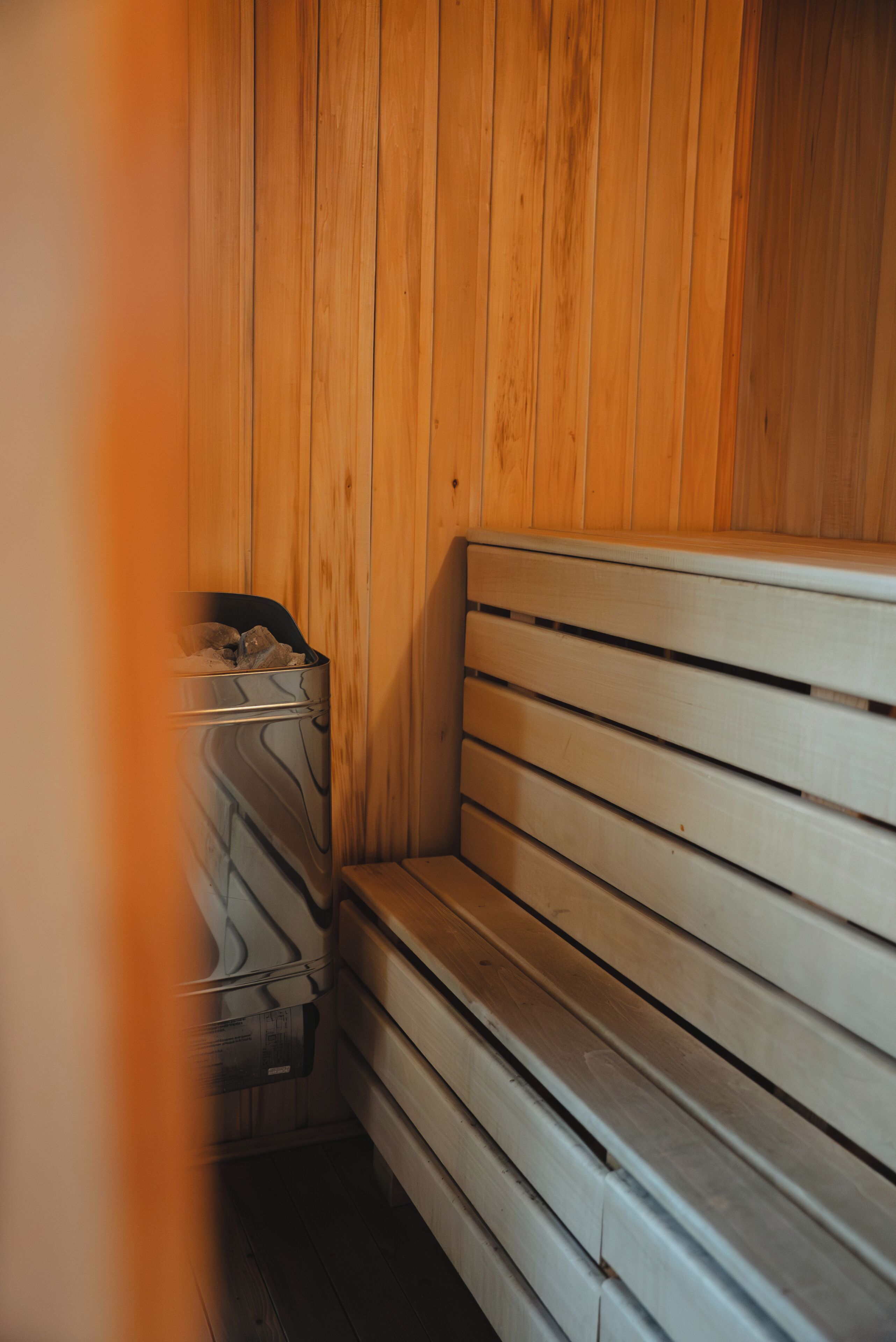 A wooden bench with a metal trash bin in a sauna room.