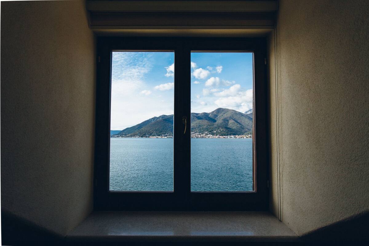 A window with a view of a calm sea and distant mountains.