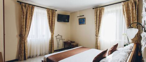 Habitación de hotel con una cama grande, un televisor de pantalla plana montado en la pared y una mesita con una silla.