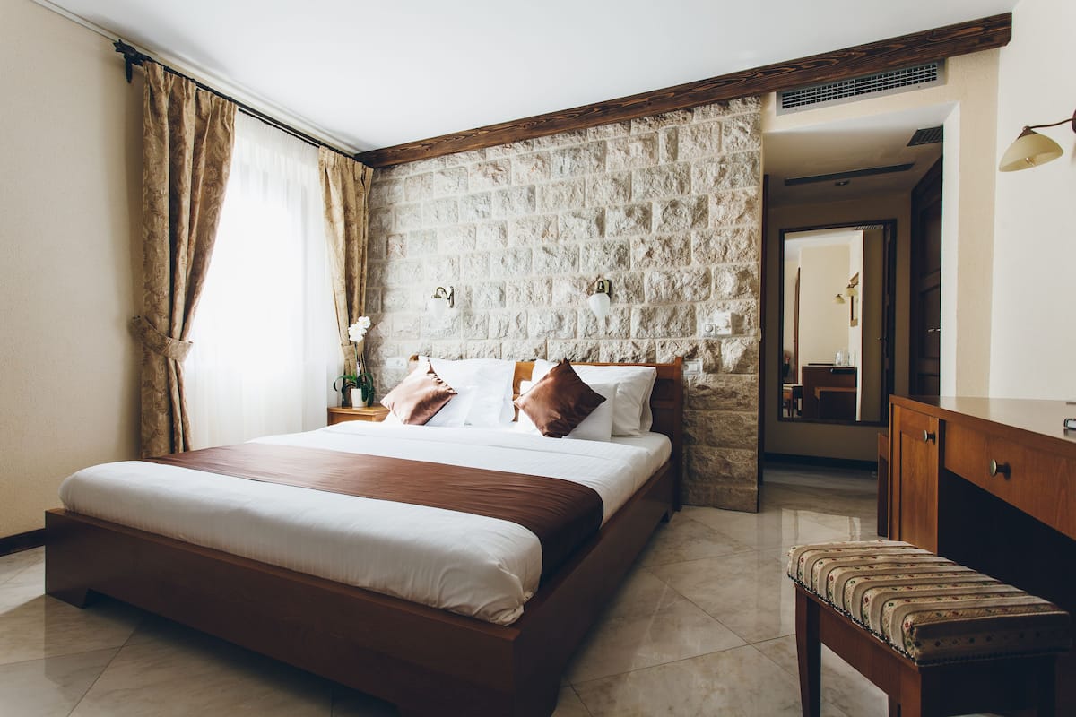 A bedroom with a stone wall, a wooden bed, a bench, and a mirror.