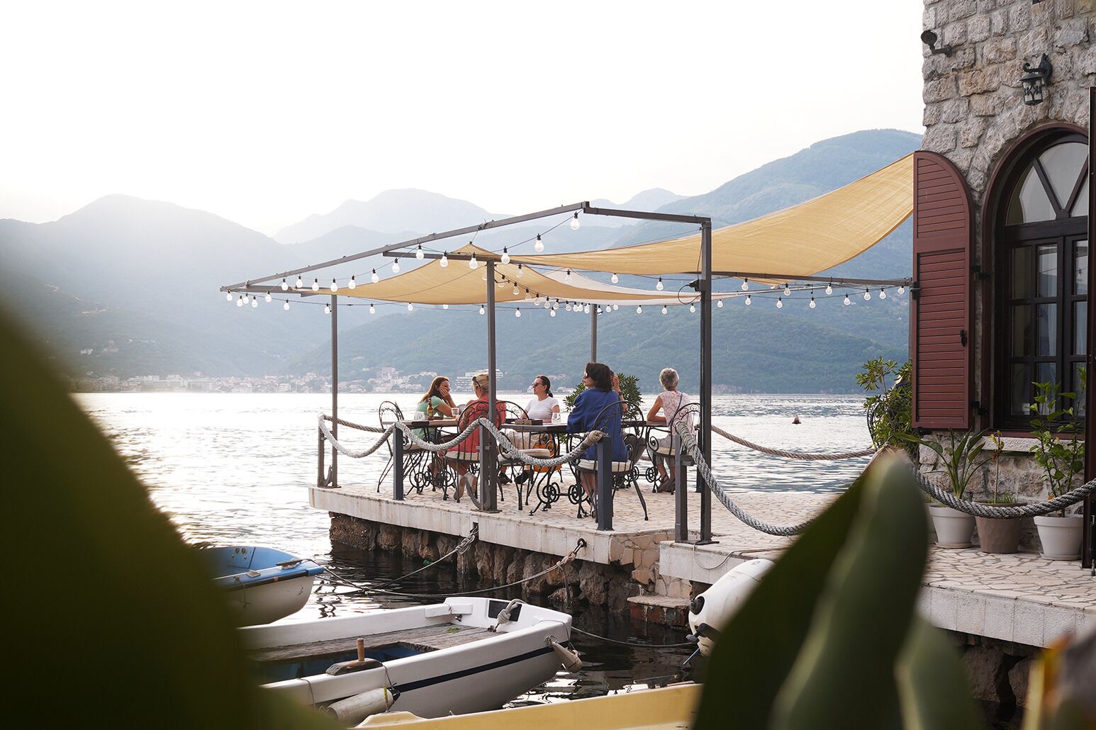 Una terraza con mesas y sillas, con vista a un cuerpo de agua donde hay barcos amarrados.