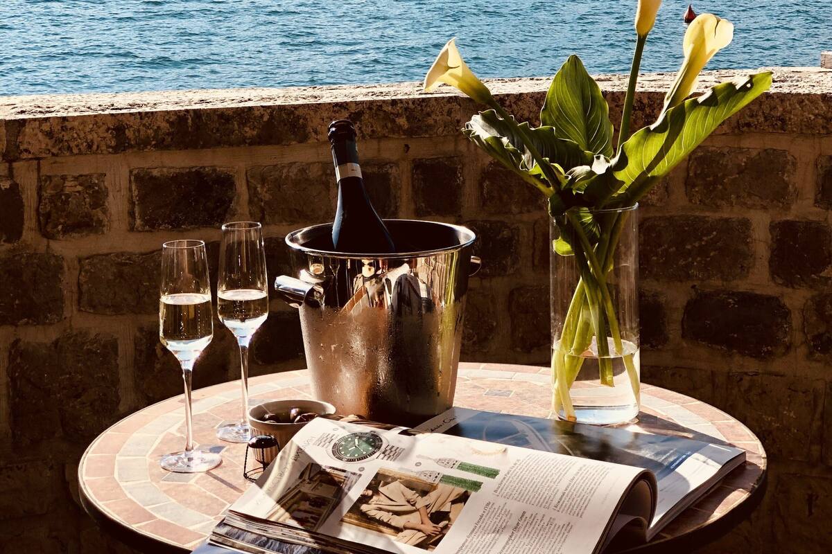A table with a bottle of champagne, two glasses, a vase with flowers, and a newspaper.