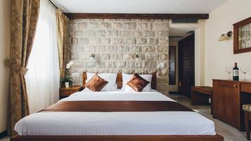 A bedroom with a stone wall, wooden bed frame, and a nightstand with a lamp.