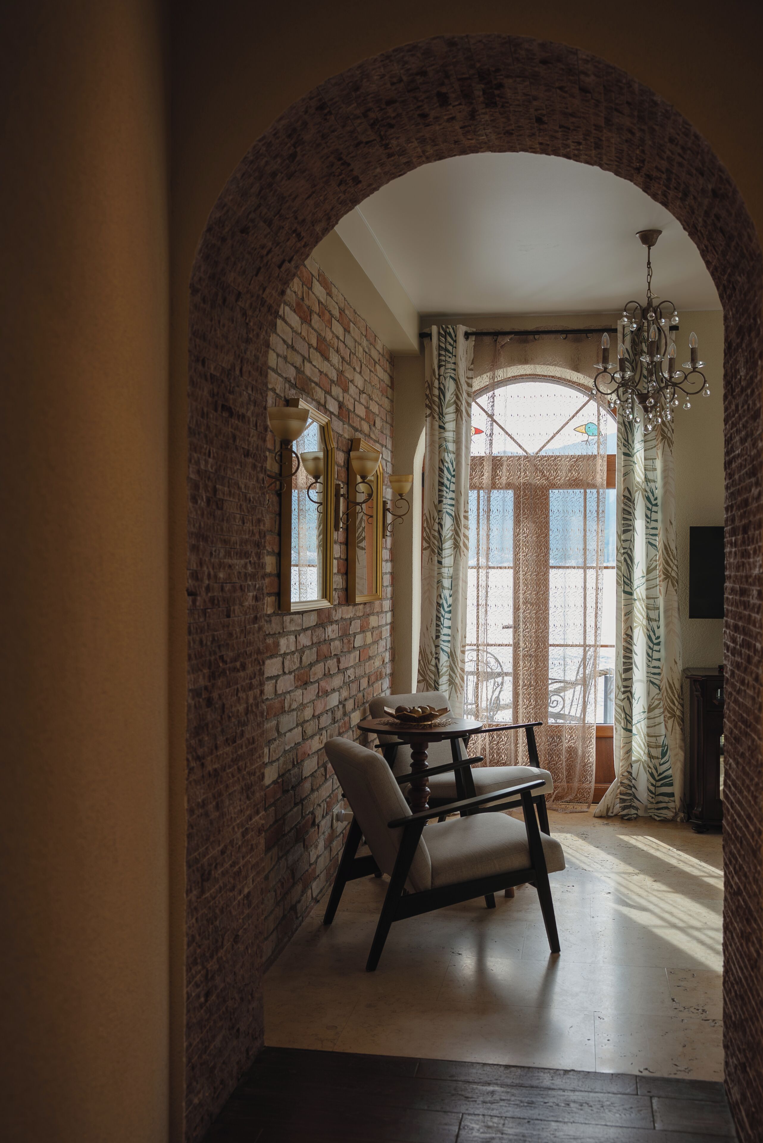 A hallway with a brick wall, a wooden chair, a table, and a chandelier.