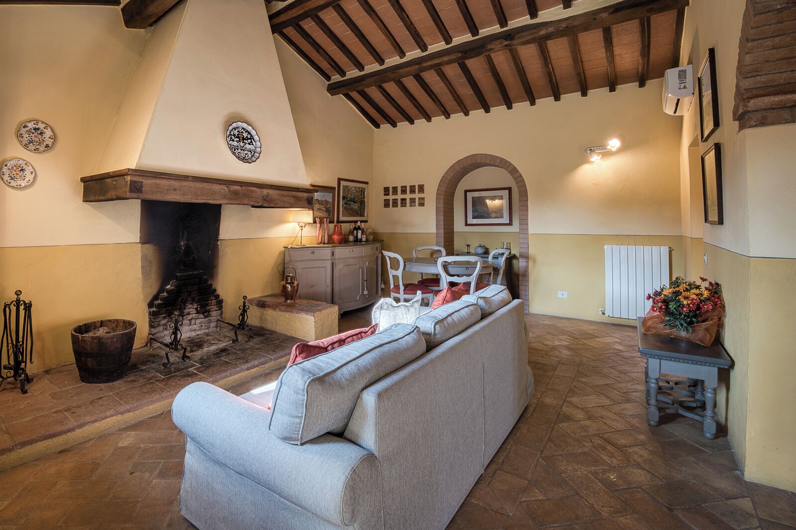 Uma sala de estar acolhedora com lareira, um sofá, uma mesa de jantar e um arranjo de flores.