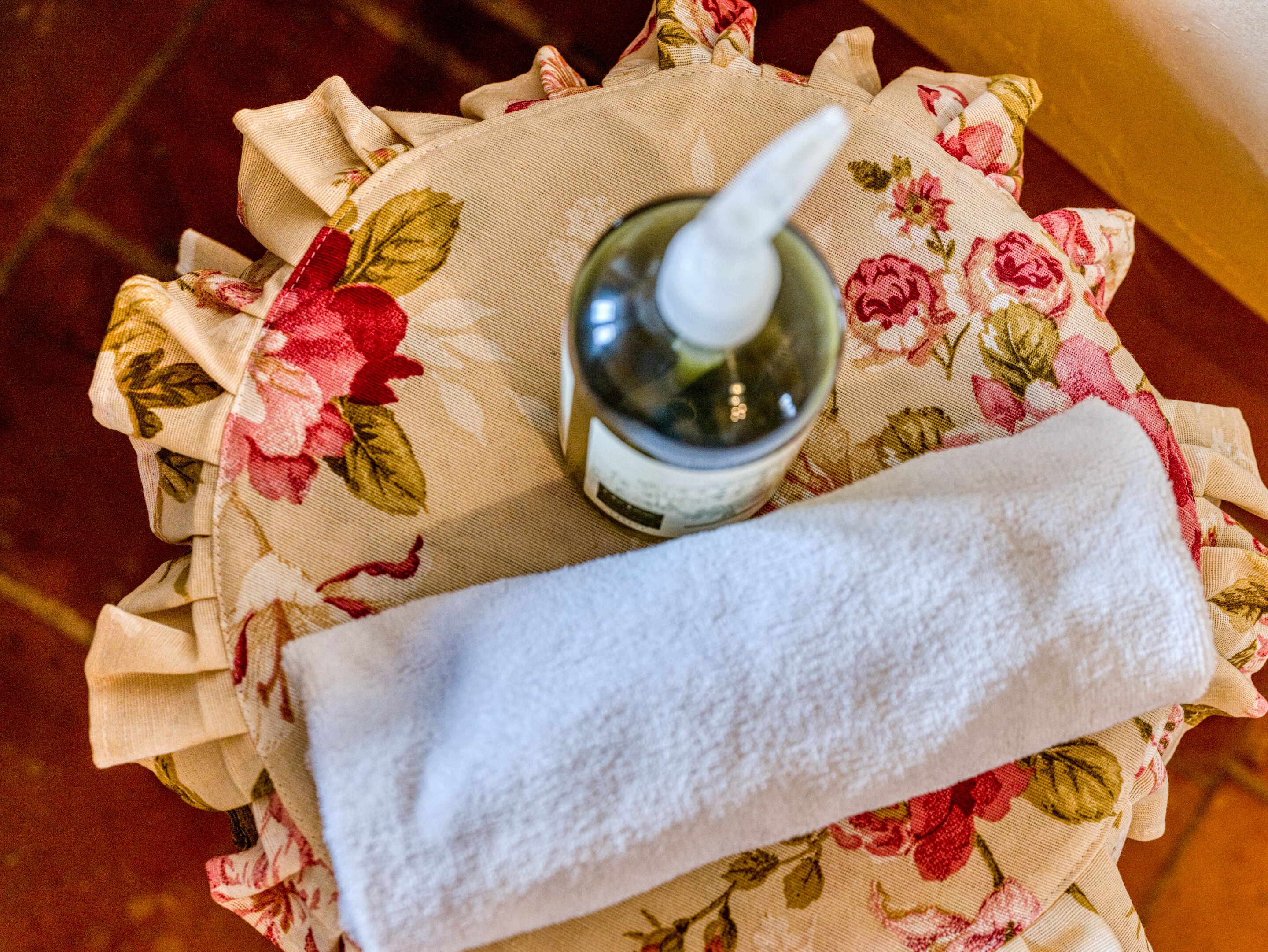 A bottle of hand sanitizer and a white towel on a floral-patterned cloth.