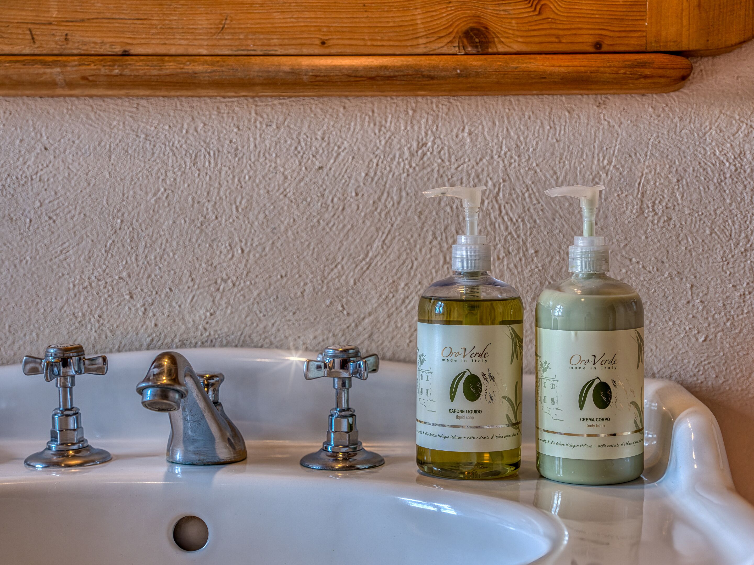 A bathroom sink with two bottles of Oro Verde body lotion and two faucets.
